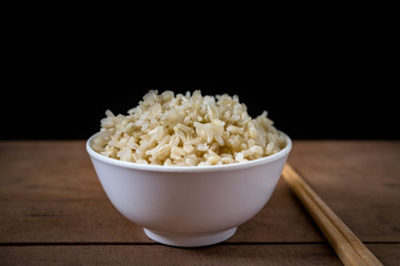 Steamed organic brown rice in the white bowl with wooden chopsticks on wooden table background