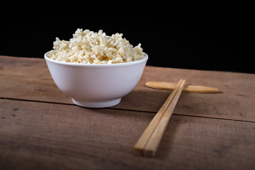 Steamed organic brown rice in the white bowl with wooden chopsticks on wooden table background