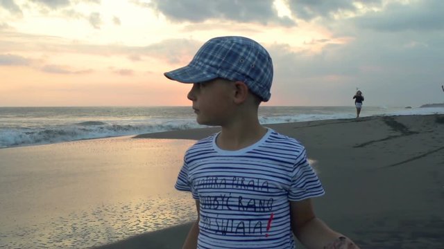 Small boy standing on the beach and looks happy, steadycam shot, slow motion shot at 240fps
