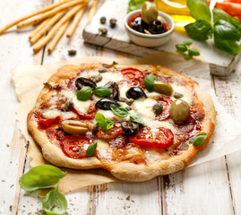 Homemade pizza with tomatoes, olives, salami, mozzarella cheese and fresh basil on a wooden rustic...