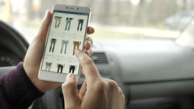 A man looks at the goods in the online clothing store, sitting in the car. Smart phone online shopping.