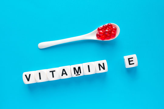 Red capsules in the white spoon and the word vitamin E from white cubes with letters on a blue background. healthy and medical concept. Tocopherols and tocotrienol health benefits