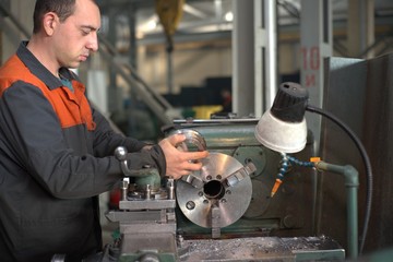 metalworking industry: factory man worker in uniform working on lathe machine in workshop
