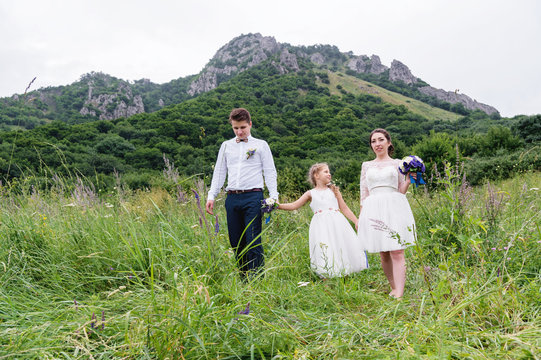 A young couple and their daughter in wedding dresses are walking in nature
