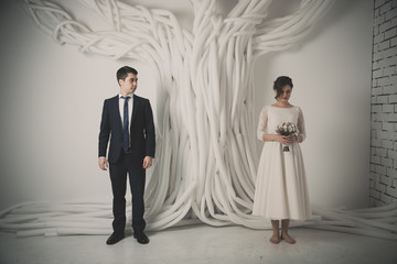 Wedding couple stand behind plastic tube tree, near brick wall relationship concept