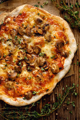 Homemade pizza with mushrooms, mozzarella cheese and fresh thyme on a wooden table, top view