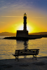 Sunrise view from a bench  at the port of Chania Crete in Greece. Sun rises behind the lighthouse of the port