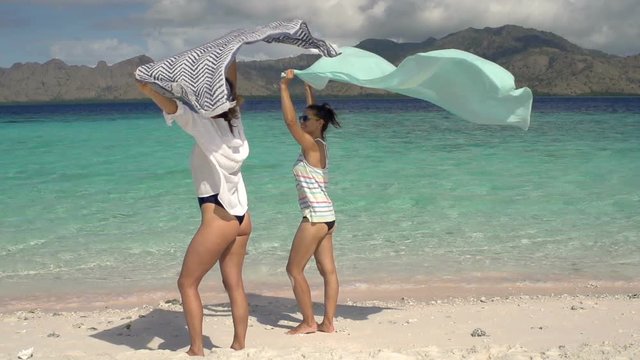 Women standing on the beautiful beach and holding scarfs, steadycam shot, slow motion shot at 240fps
