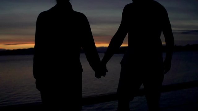Couple holding each other hands and admires the sea at night, steadycam shot, slow motion shot at 240fps
