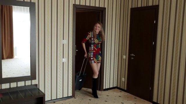 A young woman walks in with a suitcase in the room