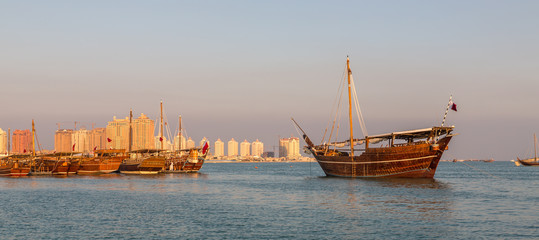 Traditional wooden boats dhow in Katara beach in Doha,Qatar Daylight view with Qatar flag and skyline in background - obrazy, fototapety, plakaty