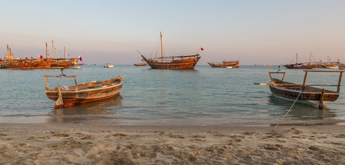 Traditional wooden boats dhow in Katara beach in Doha,Qatar Daylight view with Qatar flag 