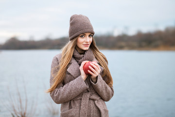 girl in a knitted cap and scarf with an apple in the fall on nature.