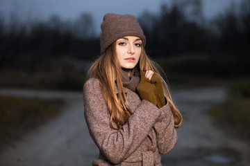 girl in a knitted hat and scarf freezes in the evening in the autumn on the nature.