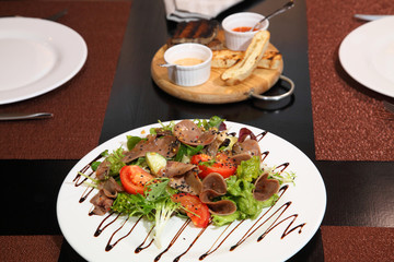Salad with beef tongue with vegetables and herbs, dressed with sauce on a white plate.