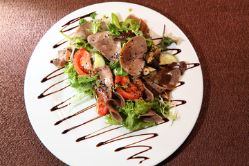 Salad with beef tongue with vegetables and herbs, dressed with sauce on a white plate.
