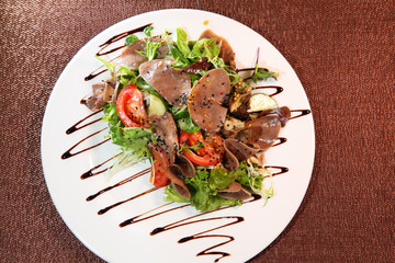 Salad with beef tongue with vegetables and herbs, dressed with sauce on a white plate.