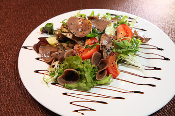 Salad with beef tongue with vegetables and herbs, dressed with sauce on a white plate.