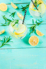 Cold lemonade or alcohol vodka cocktail with lemon and rosemary, on light blue table, copy space top view