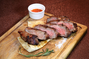 Medium-roasted steak cut into pieces on a wooden board with sauce and seasonings.