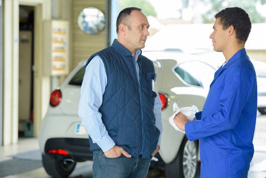 maintenance engineer talking to male customer in car repair shop