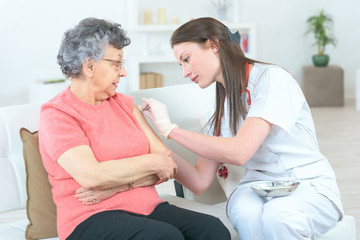 female doctor giving an injection to her elderly patient