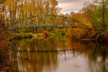 Fall colors and a bridge reflect on a quiet river