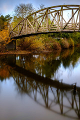 Fototapeta premium Fall colors and a bridge reflect on a quiet river