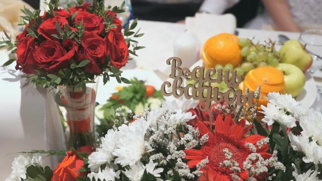 Close-up wedding table of unidentified newlyweds with bouquets and inscription in Russian - On Wedding Day