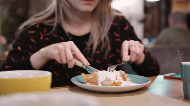Unrecognizable girl eating orange dessert strudel at the restaurant using fork and knife. Slow motion.