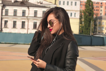 Fototapeta premium Closeup portrait of smiling brunette woman watching video on mobile telephone, standing at the street