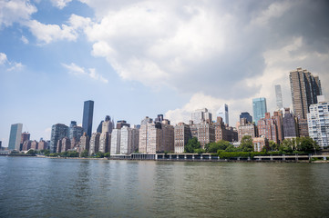New York City skyline viewed across the East River from Roosevelt Island waterfront.