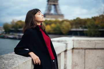 Beautiful young Parisian woman in long coat near the Eiffel tower on a autumn day