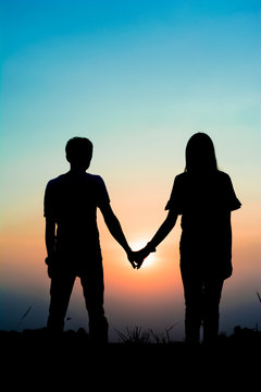 silhouette of a couple lovers holding hand at the sunset time on meadow looking at the sun . Have a beauty pink and blue sky.