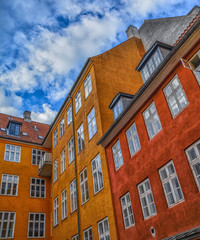 The courtyard with bright orange and red typical scandinavian houses against the blue sky with clouds. Geometry. Bottom view.