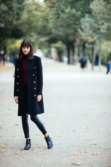 Fototapeta premium Beautiful fashion young woman in black coat walking in Paris on a autumn day