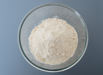 Close up shot of pile of white cake wheat flour in glass mixing bowl prepared for baking on blue background