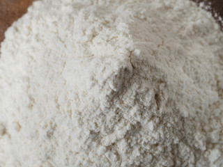 Close up shot of pile of white bread wheat flour in glass mixing bowl prepared for baking on wooden background