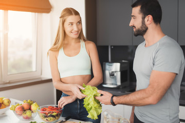 A couple is preparing a salad for breakfast. A girl cuts vegetables for a salad and a man helps her.