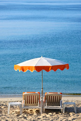 Fototapeta premium Luxury tropical caribbean beach resort sunbathing umbrella and lounger chair on sand deep blue sea summer holiday vacation photo vertical