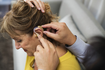 Naklejka premium A doctor inserting hearing aid to a patient's ear