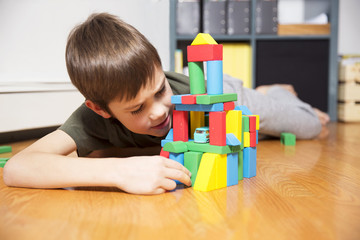 boy lying on the floor and playing with blocks. child builds buildings from colorful wooden blocks