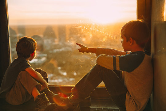 children sitting on the windowsill. Two boys looking out the window at the top of a skyscraper
