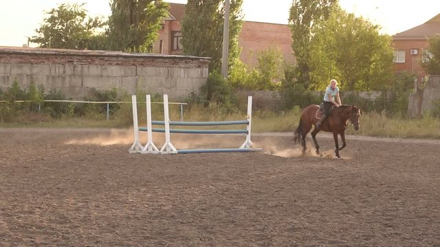 Professional rider on a horse jumps over a barrier. Competitive rider training jumping over obstacles at sunset. Mare jumps over barriers in training at the racetrack. Slow motion.