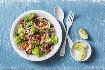 Salad with boiled chicken, tomatoes, cucumbers, lettuce, red onion and spicy ranch dressing on a blue background, top view