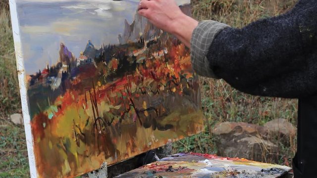 Professional artist paints a picture on canvas using oil paints. Landscape Oil Painting. Autumn vineyard. Sea. Mountains