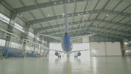Airplane in hangar, rear view of aircraft and light from windows. Large passenger aircraft in a hangar on service maintenance - obrazy, fototapety, plakaty