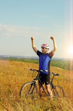 Mid age Male cyclist shows raised up hands gesture on the top of the hill
