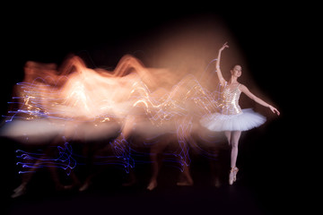 Young female / woman / girl ballerina in a white pack / tutu solo dancing doing stand on toes and leaves light leak trail of silhouette in black scene with reflecting floor and dark background © Monstar Studio