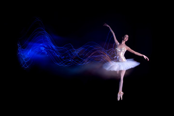 Young female / woman / girl ballerina in a white pack / tutu solo dancing doing stand on toes and leaves blue light leak trail of silhouette in black scene with reflecting floor and dark background